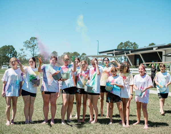 Group of young people in white shirts covered in coloured chalk and throwing it up in the air