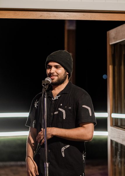 Man with a black beanie and shirt with a beard rapping into a microphone