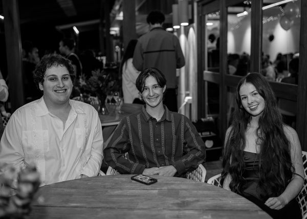 A black and white photo of three teenagers, two males and one female sitting at a table smiling