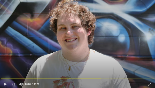 Image of a young Caucasian male in a white shirt smiling in front of a grafitti wall