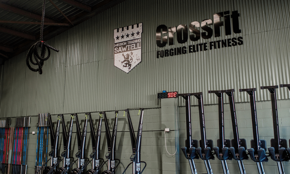 Image of inside of a crossfit gym with a rope hanging, machines and crossfit signage